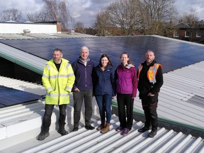 Photo of GMCR directors Ali and Kate with Wellington School CFO Gemma Tunstall and NPS staff standing on top of the school roof with solar panels behind them