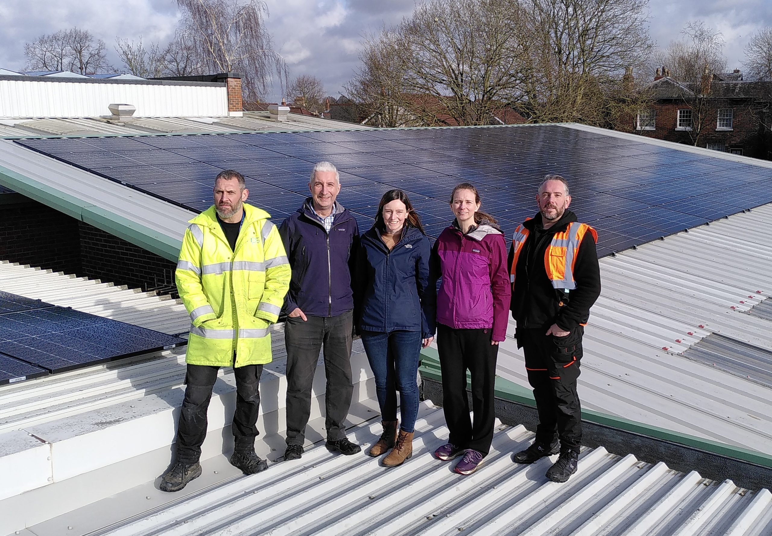 Photo of GMCR directors Ali and Kate with Wellington School CFO Gemma Tunstall and NPS staff standing on top of the school roof with solar panels behind them